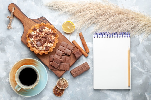 Bovenaanzicht romige kleine cake met chocoladerepen blocnote en kaneel op licht bureau zoete cake crème chocolade