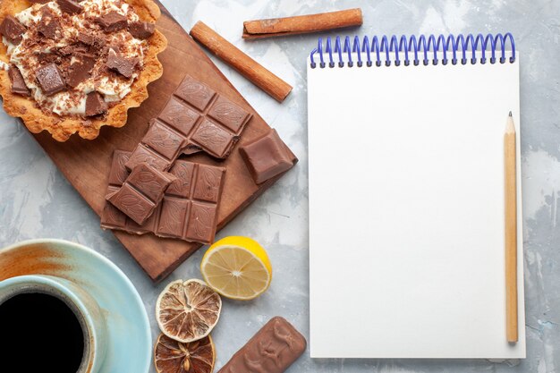 Bovenaanzicht romige kleine cake met chocoladerepen blocnote en kaneel op licht bureau zoete cake suiker crème chocolade