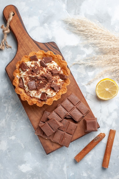 Bovenaanzicht romige kleine cake met chocoladerepen en kaneel op licht bureau zoete cake suiker crème chocolade