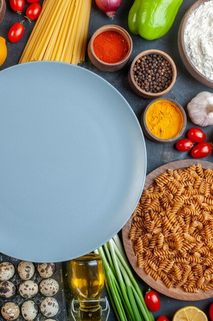 Bovenaanzicht ronde blauwe plaat met rauwe pasta groenten kruiderijen en eieren op een donkergrijze tafel eten ei deeg diner maaltijd fruit kleur