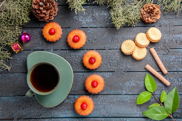 Bovenaanzicht ronde kersen cupcakes fir-tree takken kerst speelgoed kegels verschillende koekjes en een kopje thee op donkere houten tafel