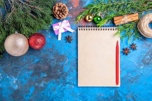 Bovenaanzicht rood potlood op een notebook pijnboomtakken op blauw oppervlak met vrije ruimte