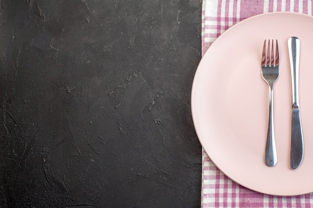 Bovenaanzicht roze plaat met mes en vork op donkere ondergrond