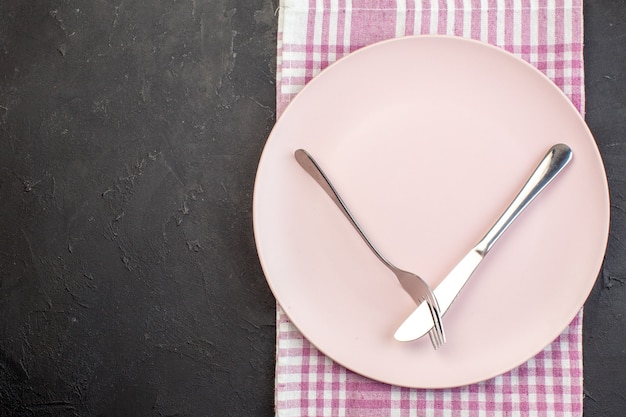 Bovenaanzicht roze plaat met mes en vork op donkere ondergrond