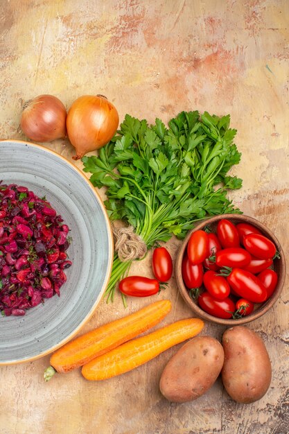 Bovenaanzicht salade op een keramische plaat met verse ingrediënten in de buurt zoals een peterselie buch kom roma tomaten wortel aardappelen en uien op een houten tafel met ruimte voor tekst