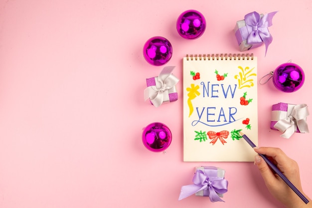 Bovenaanzicht schattige kleine cadeautjes met kerstboom speelgoed en nieuwjaarsbriefje op de roze achtergrond