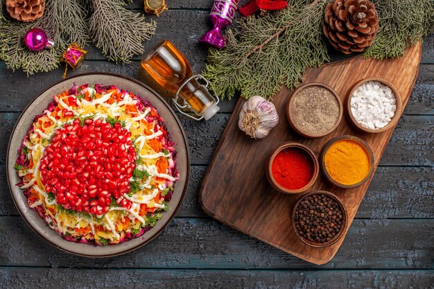 Bovenaanzicht schotel en kruidenschotel met granaatappels naast de fles olie kruiden knoflook op de snijplank en boomtakken met kegels en kerstboomspeelgoed