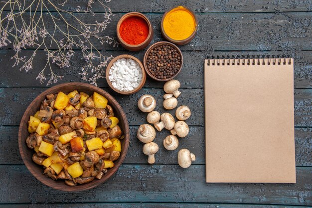 Bovenaanzicht schotel notitieboekje en kruiden schotel van champignons en aardappelen naast witte champignons kleurrijke kruiden takken en een notitieboekje