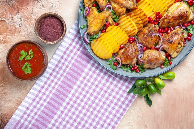 Bovenaanzicht schotel saus kruiden kippenvleugels aardappelen op het wit-paarse tafelkleed