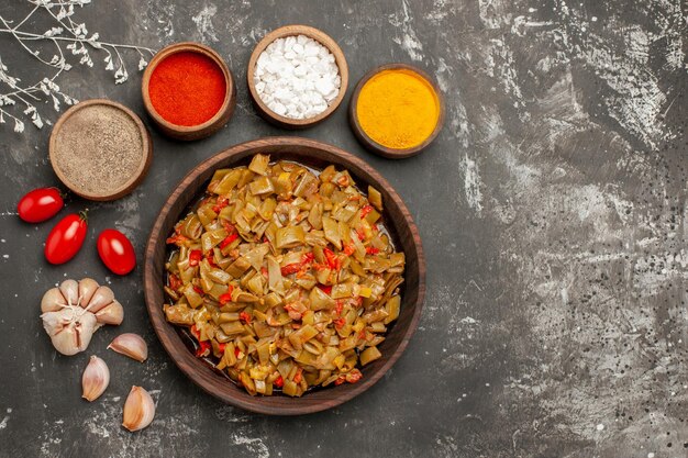 Bovenaanzicht schotel van bonen kommen met kruiden en knoflook rond het bord sperziebonen met tomaten op de zwarte tafel