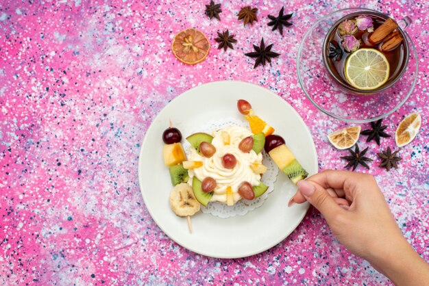 Bovenaanzicht slagroomtaart met vers gesneden fruit en thee op de gekleurde achtergrond cake koekjesdeeg bakken