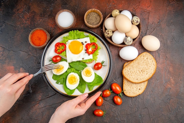 Bovenaanzicht smakelijk broodje met eieren, kruiden en tomaten op donkere tafel