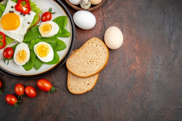 Bovenaanzicht smakelijk broodje met gekookte eieren en tomaten op donkere tafel