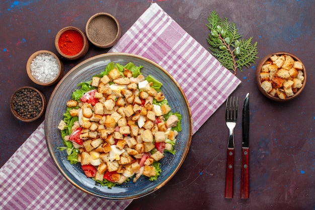 Bovenaanzicht smakelijke caesar salade met beschuit en kruiderijen op het donkere bureau