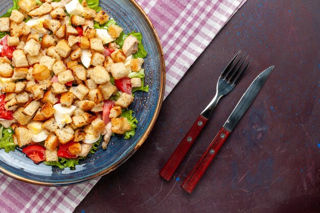 Bovenaanzicht smakelijke caesar salade met bestek op het donkere bureau