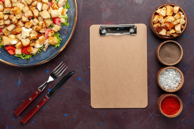 Gratis foto bovenaanzicht smakelijke caesar salade met verschillende smaakmakers op het donkere bureau