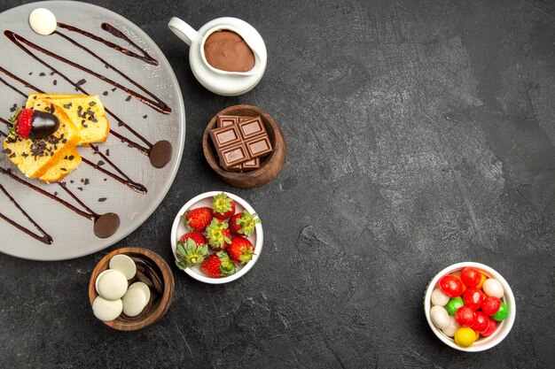 Bovenaanzicht smakelijke cake smakelijke cake met chocolade en aardbeien naast de kommen met chocolade en aardbeien aan de linkerkant en snoep aan de rechterkant van de tafel