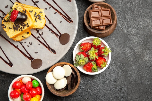 Bovenaanzicht smakelijke cake smakelijke cake met chocolade en aardbeien naast de vier kommen met snoep en bessen