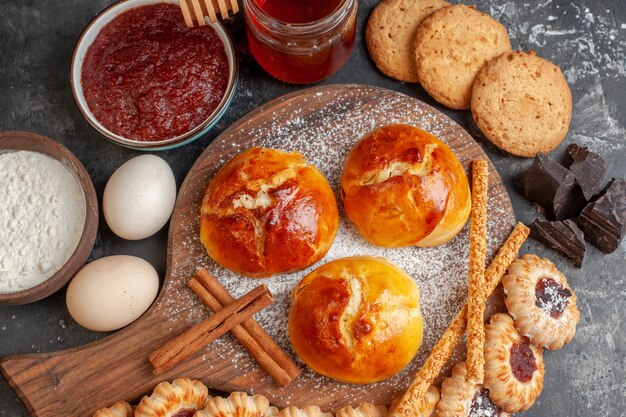 Bovenaanzicht smakelijke dinerbroodjes op houten serveerplank eieren koekjes koekjes met jam op donkere tafel