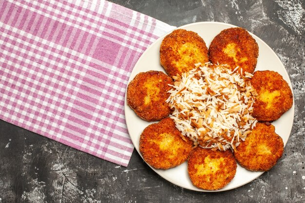 Bovenaanzicht smakelijke gebakken koteletten met gekookte rijst op een donkere ondergrond rissole vlees eten