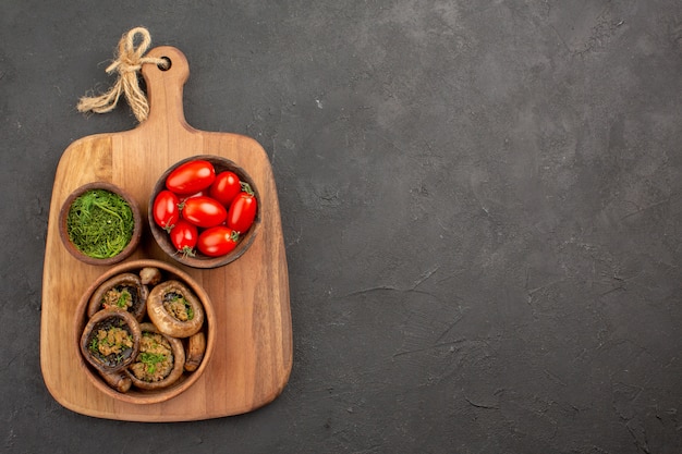 Bovenaanzicht smakelijke gekookte champignons met tomaten en greens op donkere achtergrond