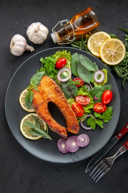Bovenaanzicht smakelijke gekookte vis met verse groenten en kruiden op de donkere tafel
