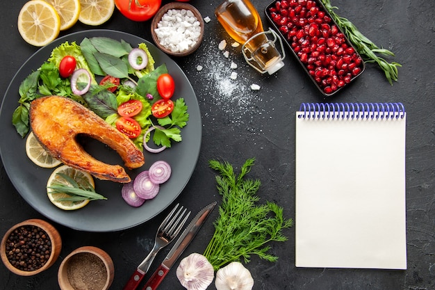 Bovenaanzicht smakelijke gekookte vis met verse groenten op de donkere tafel