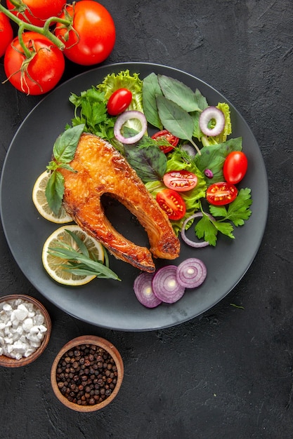 Bovenaanzicht smakelijke gekookte vis met verse groenten op donkere tafel