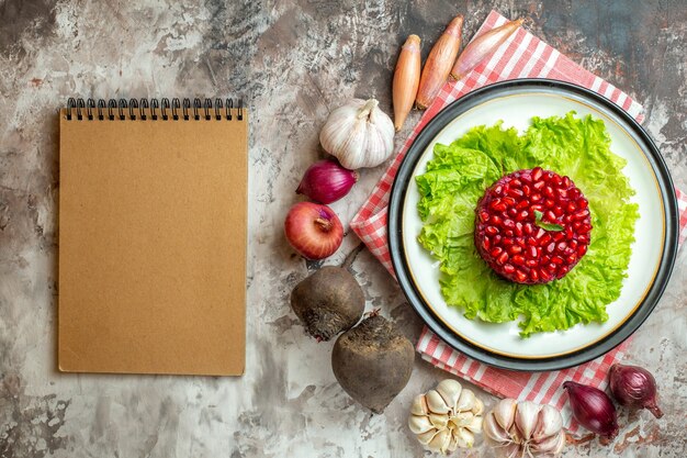 Bovenaanzicht smakelijke granaatappelsalade op groene salade met verse groenten op de lichte achtergrond