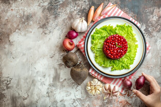 Bovenaanzicht smakelijke granaatappelsalade op groene salade met verse groenten op de lichte achtergrond