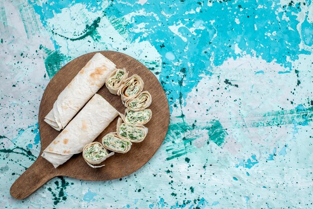 Bovenaanzicht smakelijke groentebroodjes geheel en in plakjes gesneden met greens op de blauw-lichte achtergrondkleur van het voedselmaaltijdbroodje