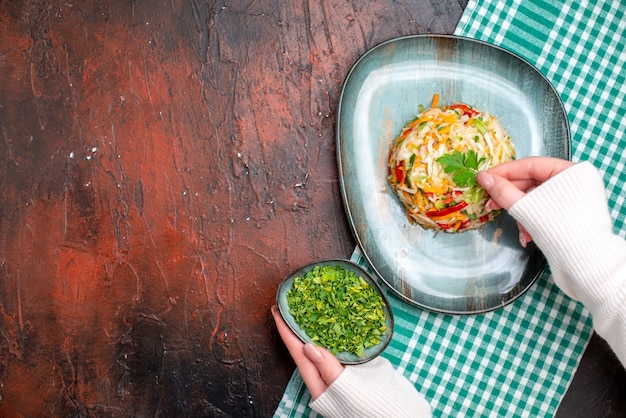 Bovenaanzicht smakelijke groentesalade in bord met vrouwelijke handen op de donkere tafel