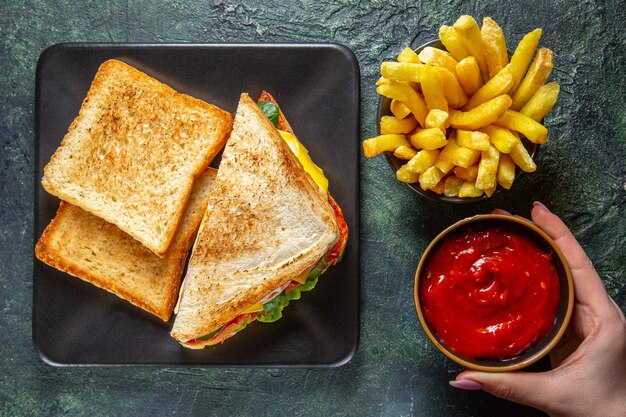 Bovenaanzicht smakelijke ham sandwiches met toast Franse frietjes en tomatenpuree op donkere ondergrond