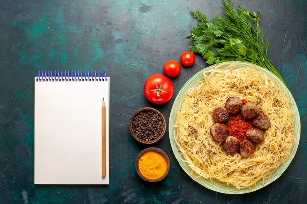 Bovenaanzicht smakelijke Italiaanse pasta met gehaktballen Kladblok en verschillende kruiden op donkerblauwe achtergrond