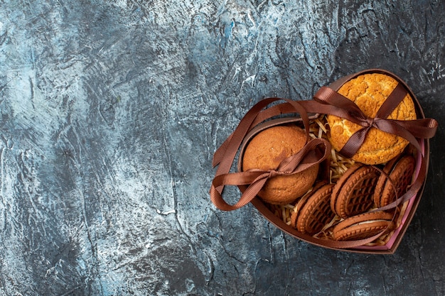 Bovenaanzicht smakelijke koekjes vastgebonden met touw in hartvormige doos op donkere achtergrond