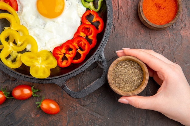 Bovenaanzicht smakelijke omelet met gesneden paprika en smaakmakers op de donkere tafel