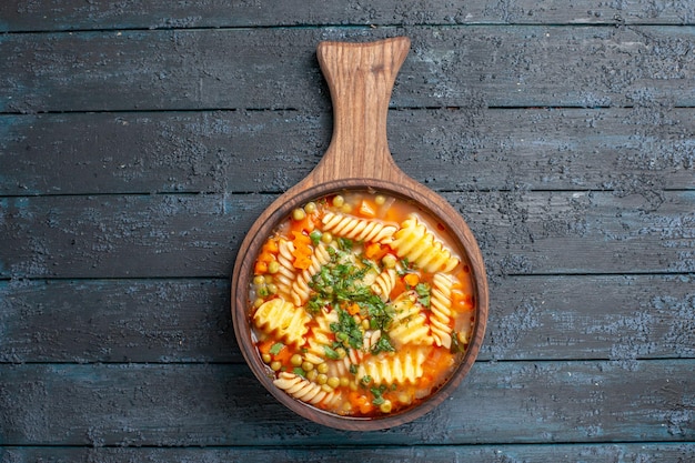 Bovenaanzicht smakelijke pastasoep van spiraalvormige italiaanse pasta met greens op donkerblauwe bureaukeukenschotel italiaanse pastasoepkleur