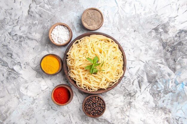 Bovenaanzicht smakelijke spaghetti met smaakmakers op een deegschotel met witte vloerdeeg pastamaaltijd