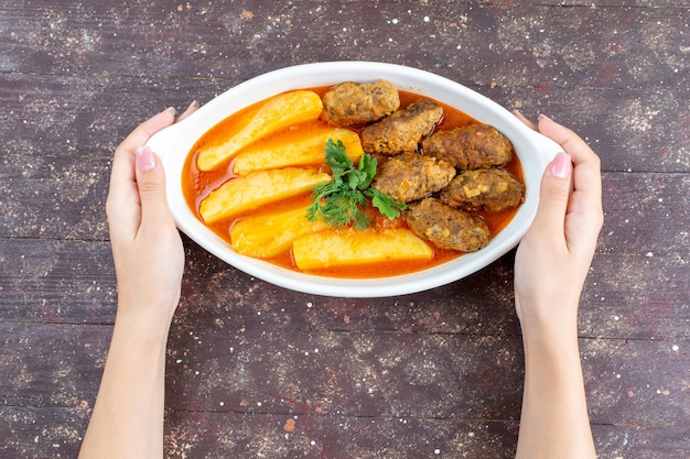 Bovenaanzicht smakelijke vleeskoteletten gekookt samen met aardappelen en saus in plaat nemen door vrouw op de bruine achtergrond vlees aardappel gerecht maaltijd diner