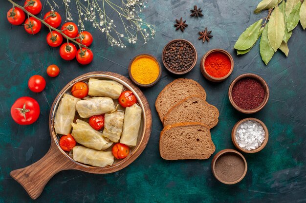 Bovenaanzicht smakelijke vleesmaaltijd gerold in kool met brood en verse tomaten op het donkerblauwe bureau