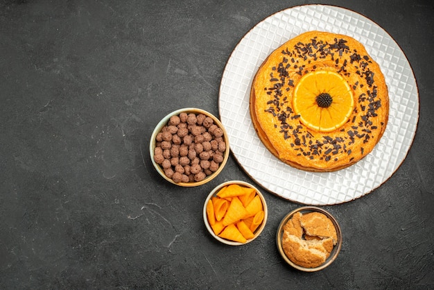 Bovenaanzicht smakelijke zoete taart met stukjes sinaasappel op donkergrijs bureau zoete taart dessert thee biscuit cake suiker