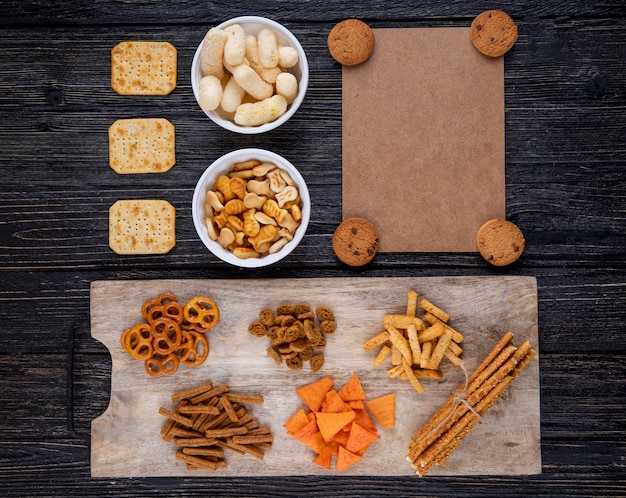 Bovenaanzicht snacks chocolade koekjes beschuiten mini brezel paprika chips cracker sticks viscrackers en maïs sticks op zwarte houten achtergrond