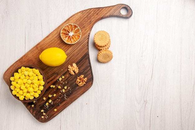 Bovenaanzicht snoep en snoep kom met snoep, noten en citroen op de snijplank naast de koekjes aan de linkerkant van de witte tafel