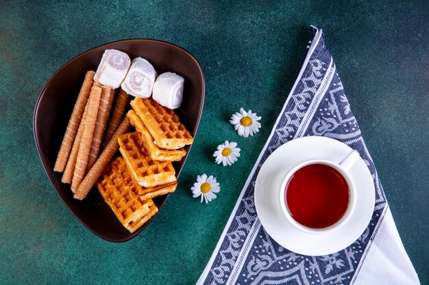 Bovenaanzicht snoep wafels zoete broodjes en marmelade met een kopje thee op groen