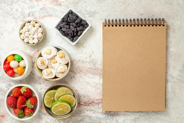 Bovenaanzicht snoepjes in kommen crème notitieboekje kommen aardbeien en snoepjes op de witte tafel