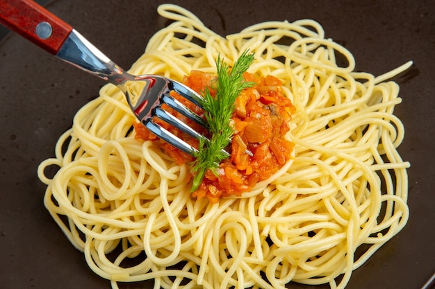 Bovenaanzicht spaghetti met saus op plaatvork op zwarte tafel