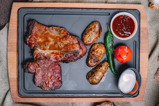 Bovenaanzicht steak in saus met aardappelen, tomaat en peper met saus op een dienblad