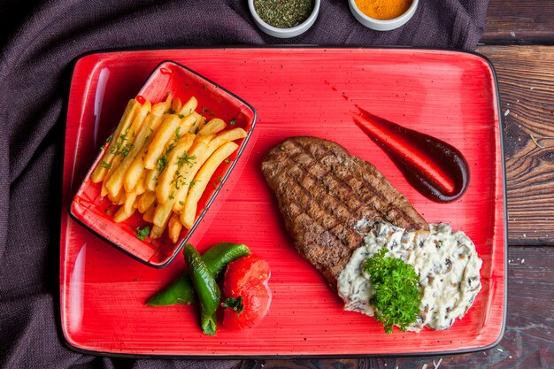 Bovenaanzicht steak steak with_fried aardappel saus, kruiden op een rode plaat