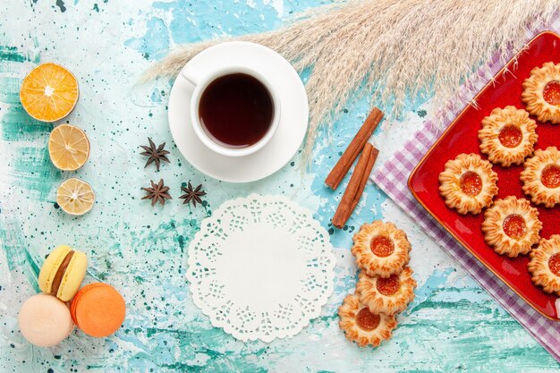 Bovenaanzicht suiker koekjes in rode plaat met kopje thee en Franse macarons op blauwe achtergrond