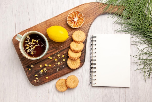 Bovenaanzicht thee en citroen een kopje thee met kruidenkoekjes en citroen op het witte notitieboekje van het keukenbord en kerstboomtakken